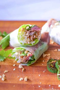 two wraps filled with meat and veggies on a cutting board next to other food items