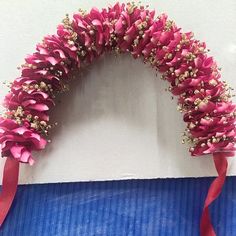 a pink flower wreath with red ribbon hanging from the wall in front of a white wall