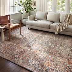 a living room with a couch, chair and rug on the floor in front of two windows