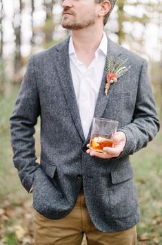 a man in a gray jacket holding a drink and wearing a flower boutonniere