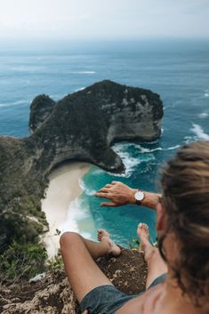 a man sitting on top of a cliff next to the ocean with his feet in the air