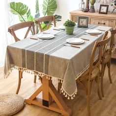 a dining room table set with place settings and plates on it, in front of a potted plant