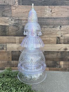 a clear glass christmas tree sitting on top of a green plant next to a wooden wall