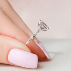 a woman's hand with a pink manicure holding a diamond ring on her finger