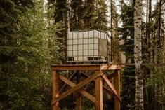 a wooden structure in the middle of a forest with trees around it and a tank on top