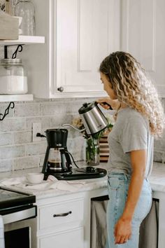 a woman standing at the kitchen counter pouring coffee into a pot with her hands on the stovetop