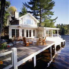 a white house sitting on top of a lake next to a wooden dock with chairs