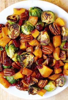 a white bowl filled with brussel sprouts and sweet potatoes on top of a wooden table