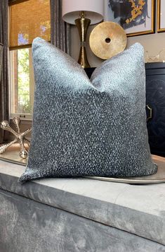 a silver pillow sitting on top of a bed next to a lamp