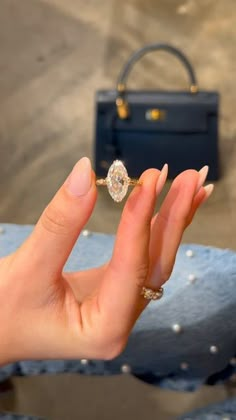 a woman's hand holding an engagement ring in front of a black box bag