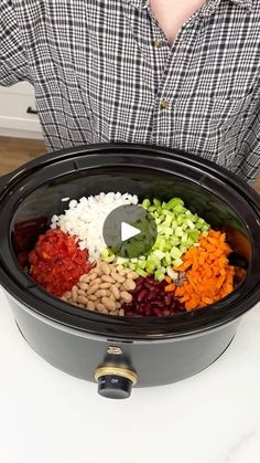 a man standing in front of a crock pot filled with beans and veggies