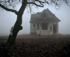 an old house in the middle of a field on a foggy, overcast day