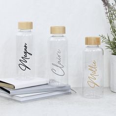 three glass bottles with writing on them sitting next to a book and plant in a vase