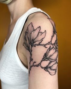 a woman wearing a white tank top with black ink on her arm and flowers in the middle