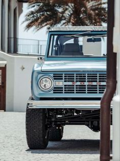 an old blue truck parked in front of a white building with palm trees behind it