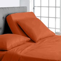 an orange sheet set on top of a bed with two pillows and a pillow case