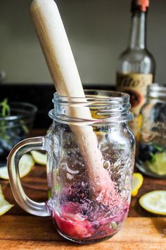 a wooden spoon sticking out of a jar filled with liquid next to lemon wedges