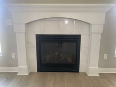 an empty living room with a fireplace in the center and white marble on the mantle