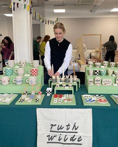 a woman standing in front of a table filled with tea cups and cake plates on it