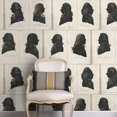 a chair sitting in front of a wall covered with black and white silhouettes on it