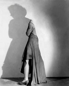 a woman standing in front of a wall with her back to the camera, casting a shadow