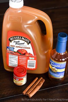 an apple cider, cinnamon sticks, and two bottles of syrup on a table