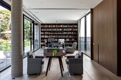 a living room filled with furniture and bookshelves next to a wall of windows