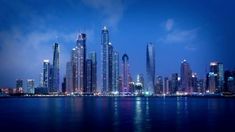 the city is lit up at night by the water with lights reflecting off it's skyscrapers