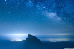 the night sky is filled with stars and bright blue light as seen from top of a mountain