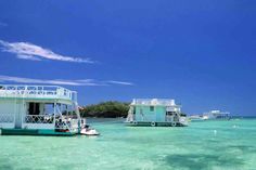 several small houses on stilts in the clear blue water near an island with boats