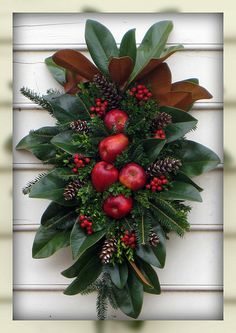 a wreath with apples and berries hanging on the side of a house window sill