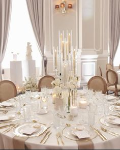 a dining room table set with white and gold plates, silverware, candles and flowers