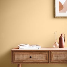 a table with two vases and books on it in front of a yellow wall