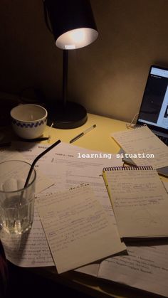 a laptop computer sitting on top of a desk next to papers and a glass filled with water