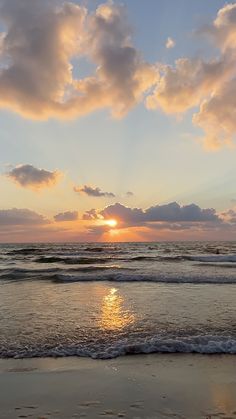 the sun is setting over the ocean with clouds in the sky and waves on the beach