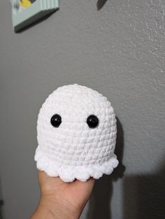 a hand holding up a crocheted white object with black eyes