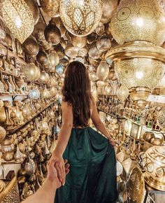 a woman in a green dress walking through a store filled with gold and silver items