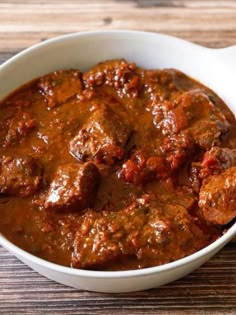 a bowl filled with meat and sauce on top of a wooden table