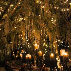 an outdoor dining area with lights strung from the trees and candles on the tables in front of it