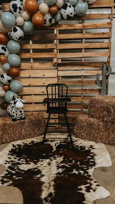 a cow hide rug in front of hay bales with balloons on the wall behind it