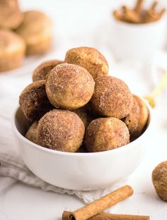 cinnamon sugar donuts in a white bowl with cinnamon sticks around them and on the table