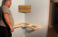 a man standing in front of a blue wall with some wooden shelves on the wall