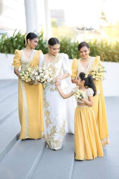 three bridesmaids in yellow and white dresses holding hands with each other on the steps