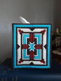 a blue, white and red crocheted square on top of a book next to a feather