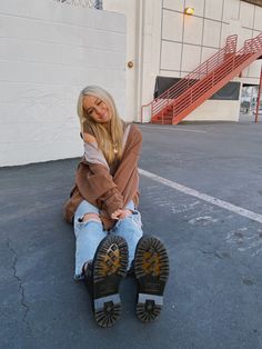 a woman sitting on the ground in front of a building with her feet propped up