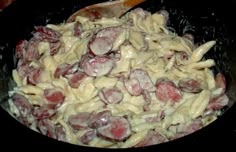 pasta with sausage and cheese in a skillet on the stove top next to a wooden spoon