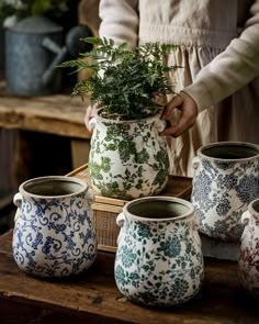 a woman is holding a potted plant in front of other pots on a table