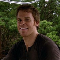 a man smiling while sitting on top of a motorcycle with trees in the back ground