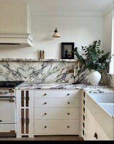 a kitchen with white cabinets and marble counter tops, an oven and sink are in the foreground