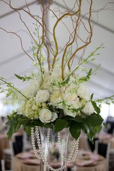 a vase filled with white flowers and greenery on top of a table under a tent